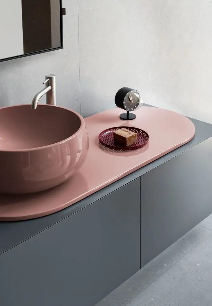 Lavabo de apoyo y top ovalado de cerámica rosa brillante sobre un mueble gris liso