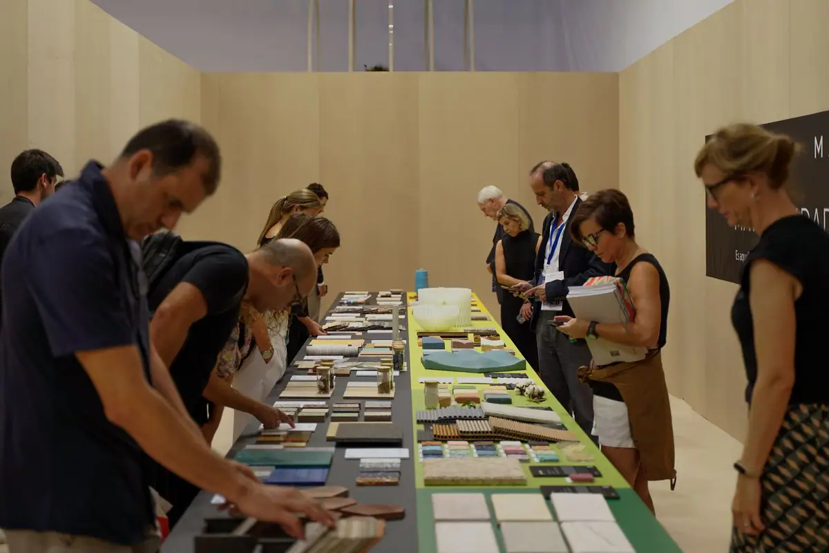 Visitantes revisan las muestras de materiales sobre la larga mesa de la exposición