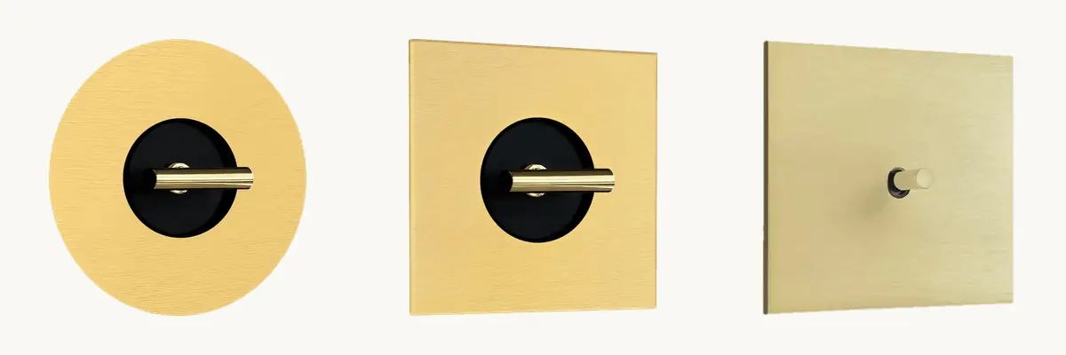 Comparativa de tres interruptores dorados: Round y Twenty con disco central negro y Atelier con placa lisa y solo la palanca.