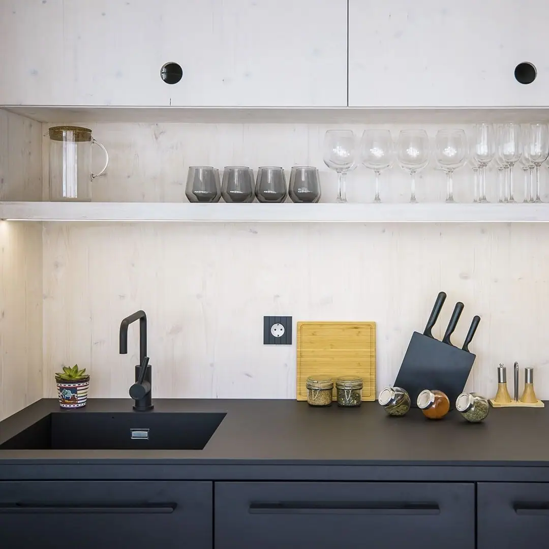 Cocina con muebles negros y frente de madera clara en el que destaca un enchufe negro de placa acanalada