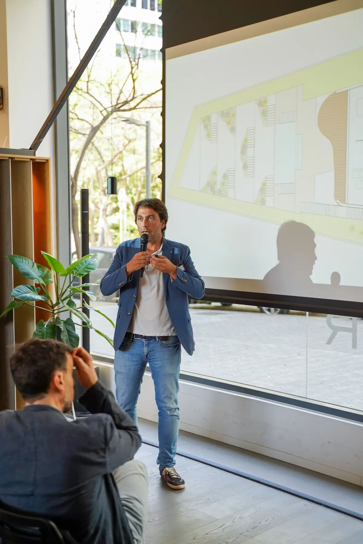 Un ponente habla ante una pantalla con un plano proyectado
