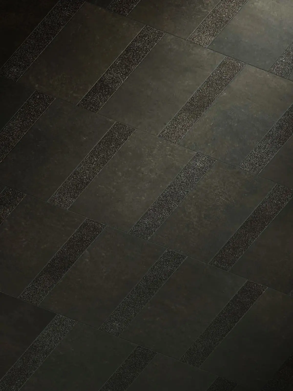 Pavimento gris muy oscuro que alterna piezas lisas y franjas con textura granulada