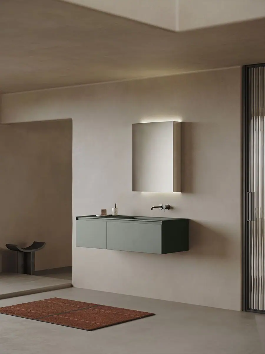 Mueble de lavabo suspendido de dos frentes en verde oscuro bajo un espejo con luz perimetral, en un baño de paredes beige