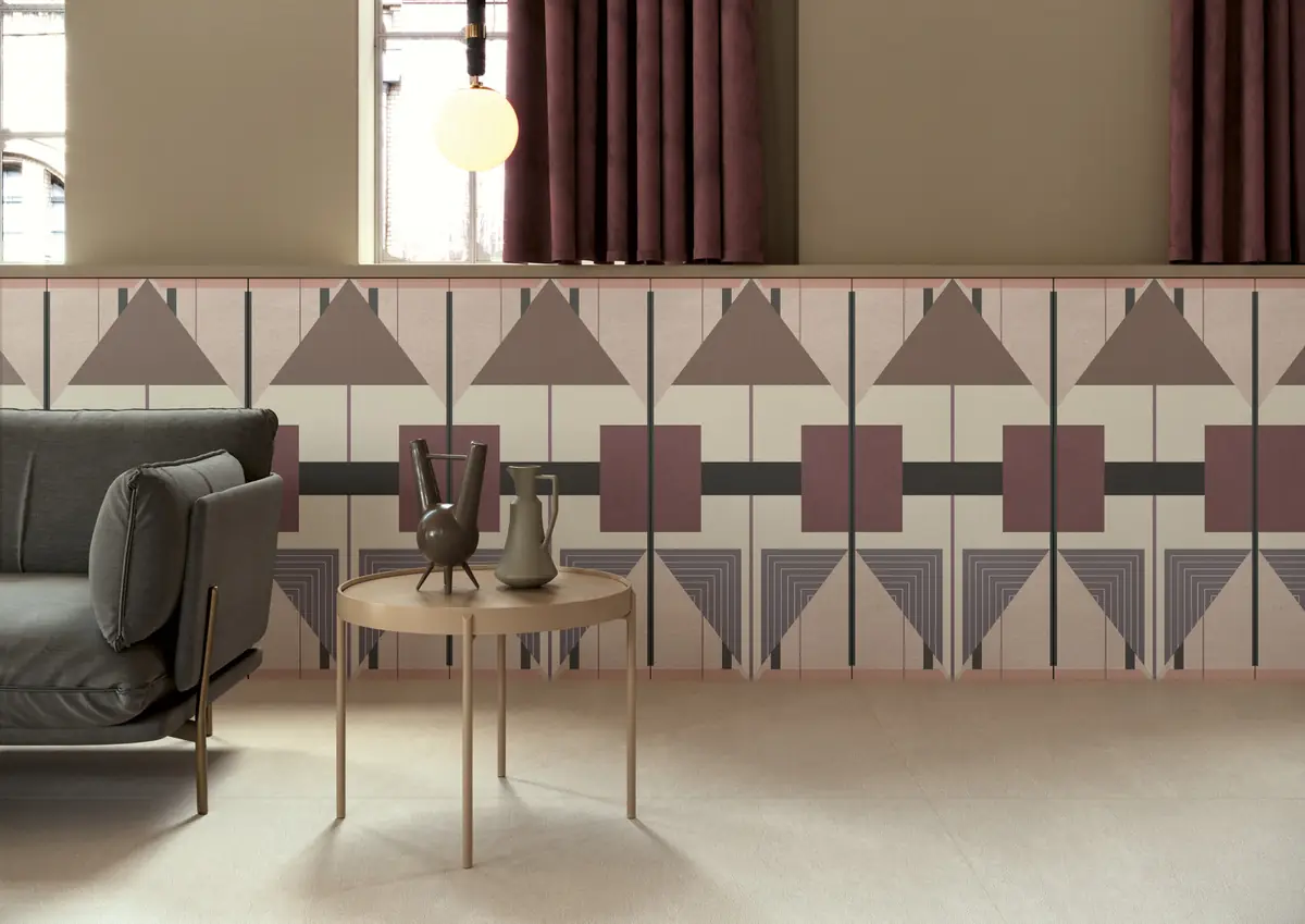 Zócalo de placas cerámicas con triángulos y rectángulos en tonos rosa, malva y gris, detrás de un sofá y una mesa auxiliar.