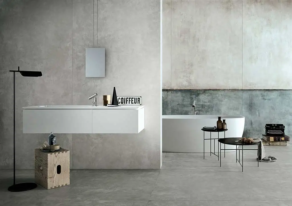Baño con lavabo suspendido y bañera ante paredes de porcelánico gris y verdoso con efecto de revoque