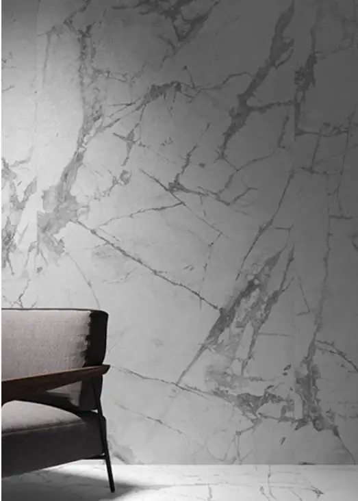 Pared revestida de porcelánico blanco efecto mármol con vetas grises y un sillón oscuro delante