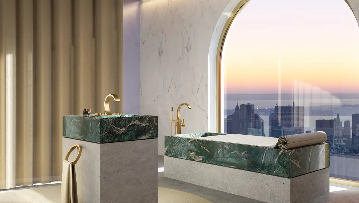 Baño con lavabo y bañera de piedra verde sobre bases de hormigón, grifería CYO dorada y gran ventanal sobre la ciudad