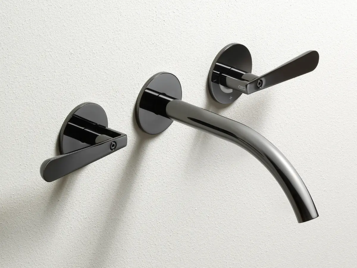Grifo de lavabo de pared con dos manetas y caño curvo en acabado negro brillante sobre una pared blanca