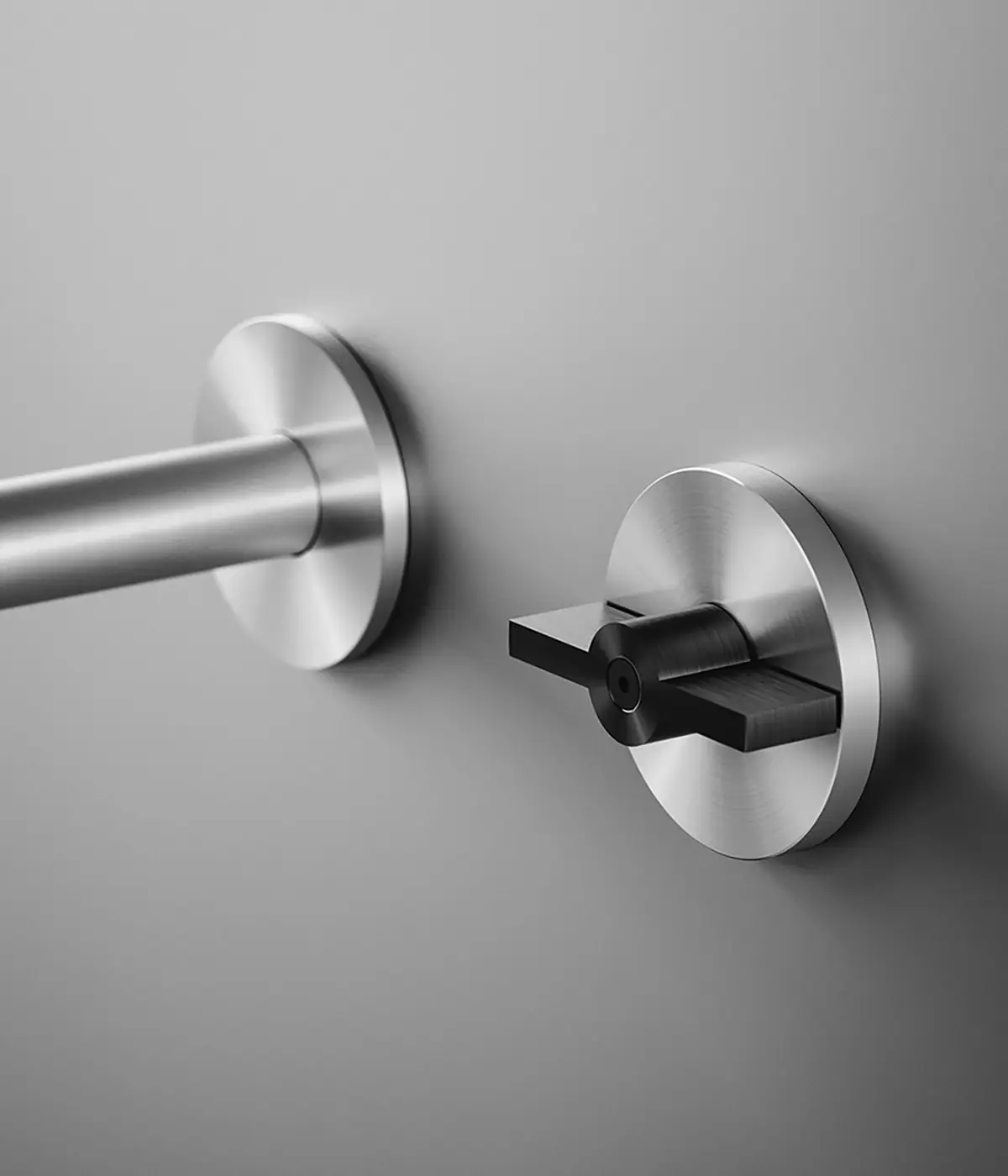 Caño de pared y mando circular de acero con maneta plana negra que recuerda a una válvula de bola
