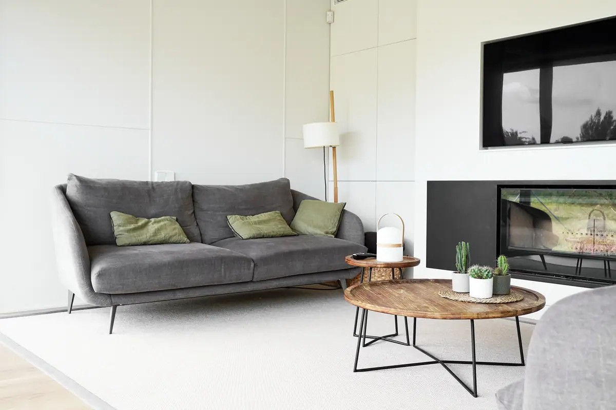 Sala de estar de la casa Om con sofá gris, mesas auxiliares de madera y chimenea empotrada en un frente blanco