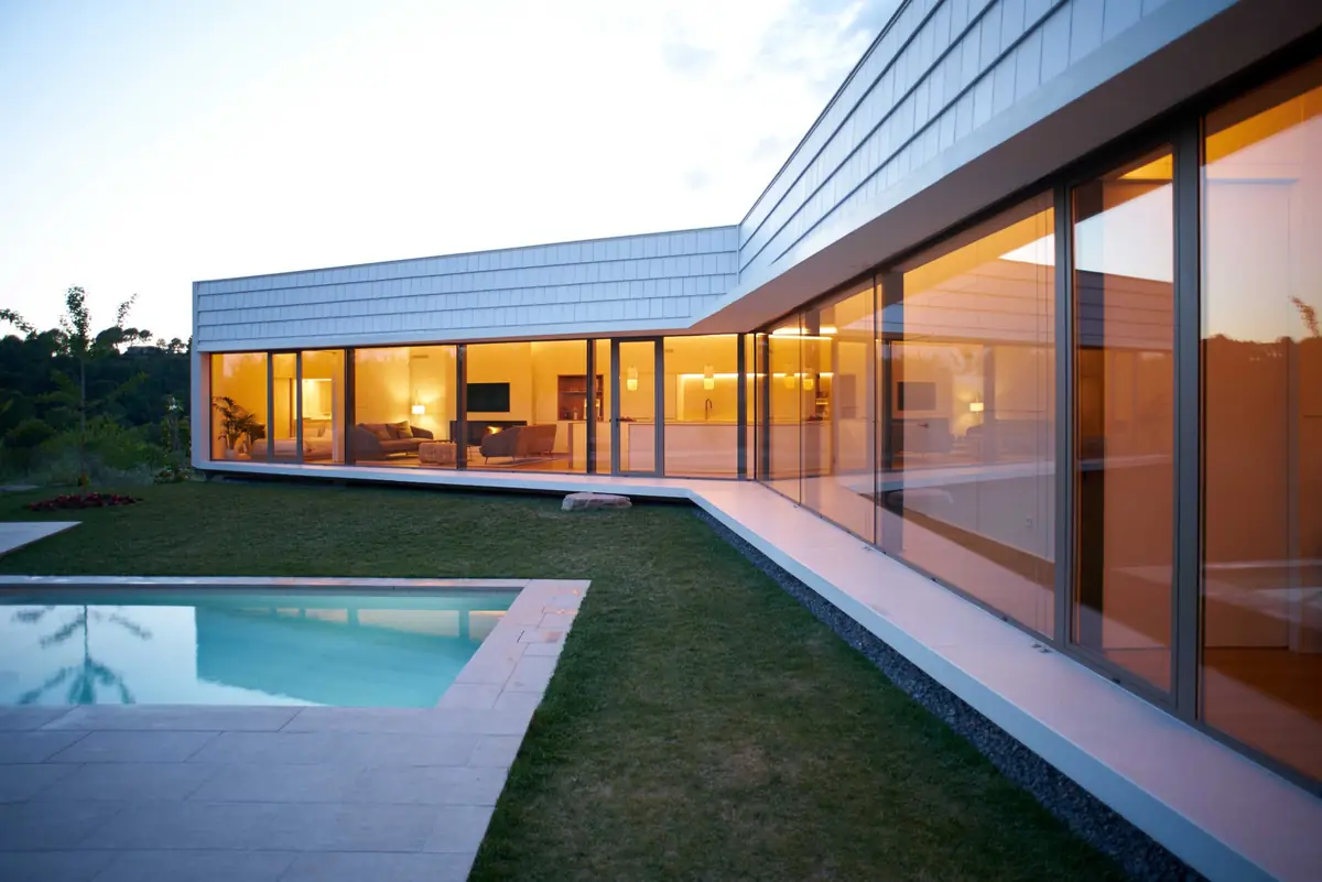 Casa Om al anochecer, con las cristaleras iluminadas que rodean el jardín y la piscina