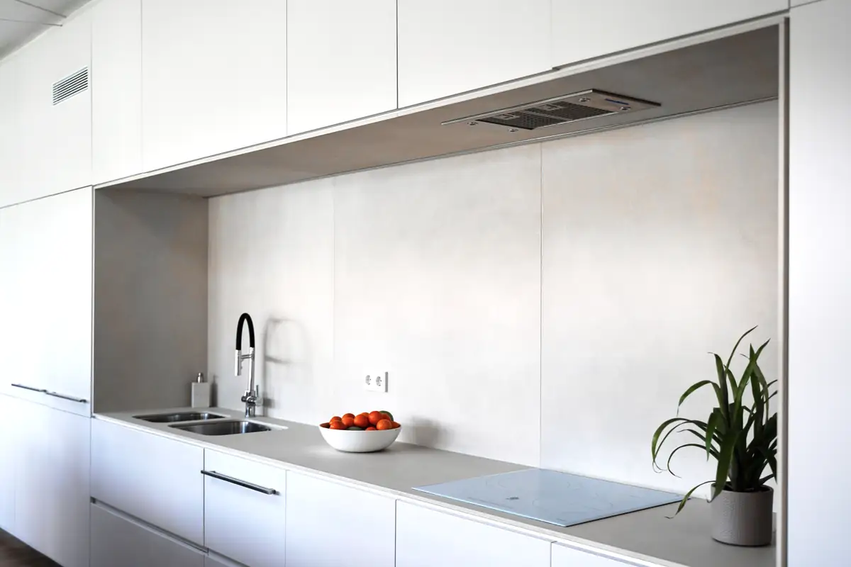 Cocina lineal blanca con hornacina revestida en tono claro, fregadero, placa de inducción y campana integrada