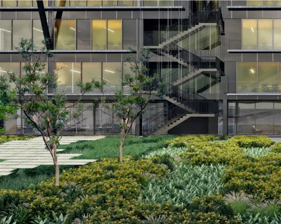 Jardín con vegetación autóctona y árboles jóvenes ante una fachada acristalada con escalera exterior.