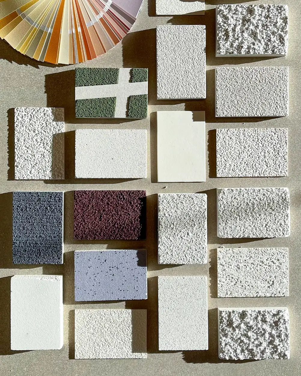Muestras de revestimientos de distintas texturas y colores junto a una carta de colores.
