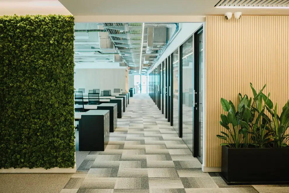 Zona de trabajo con un jardín vertical de musgo, mesas de oficina y una pared revestida con listones claros.