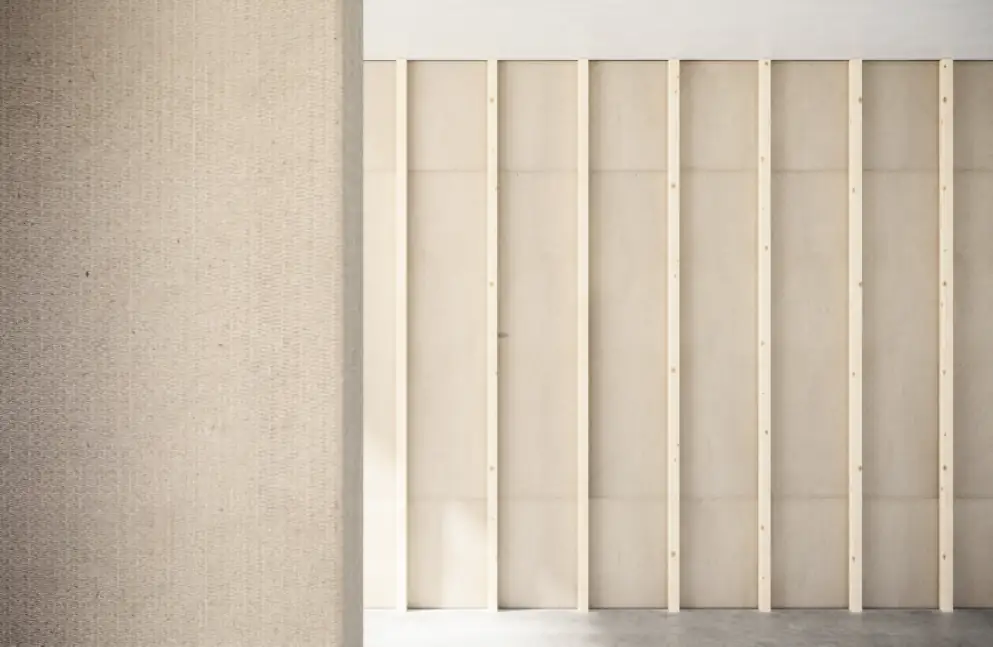 Pared revestida con un tablero beige de textura fina junto a un tabique de tableros claros sobre listones de madera.