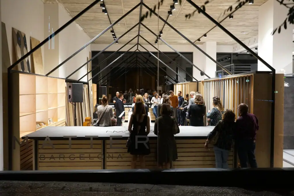Invitados alrededor del mostrador de madera de la entrada, bajo una estructura metálica en forma de casa