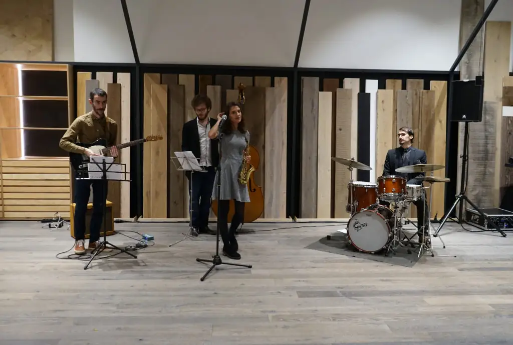 Banda de jazz con guitarra, saxofón y batería tocando ante los expositores de madera