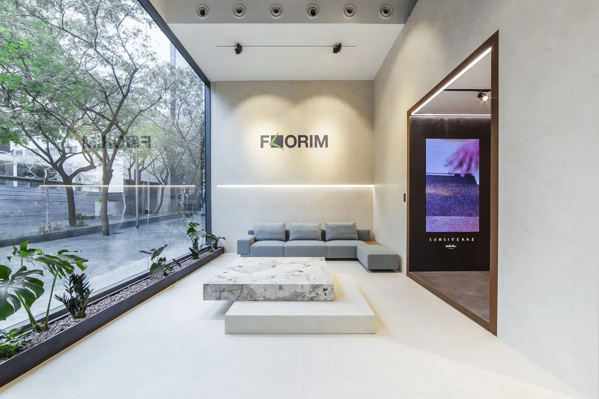 Zona de estar con sofá gris, mesa baja de piedra y logotipo de Florim frente al escaparate