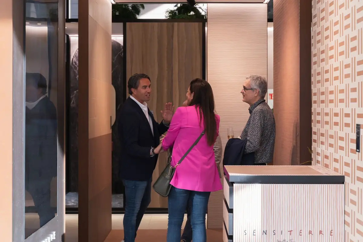 Tres asistentes conversan junto a un mueble con el rótulo SensiTerre y una pared de motivo geométrico
