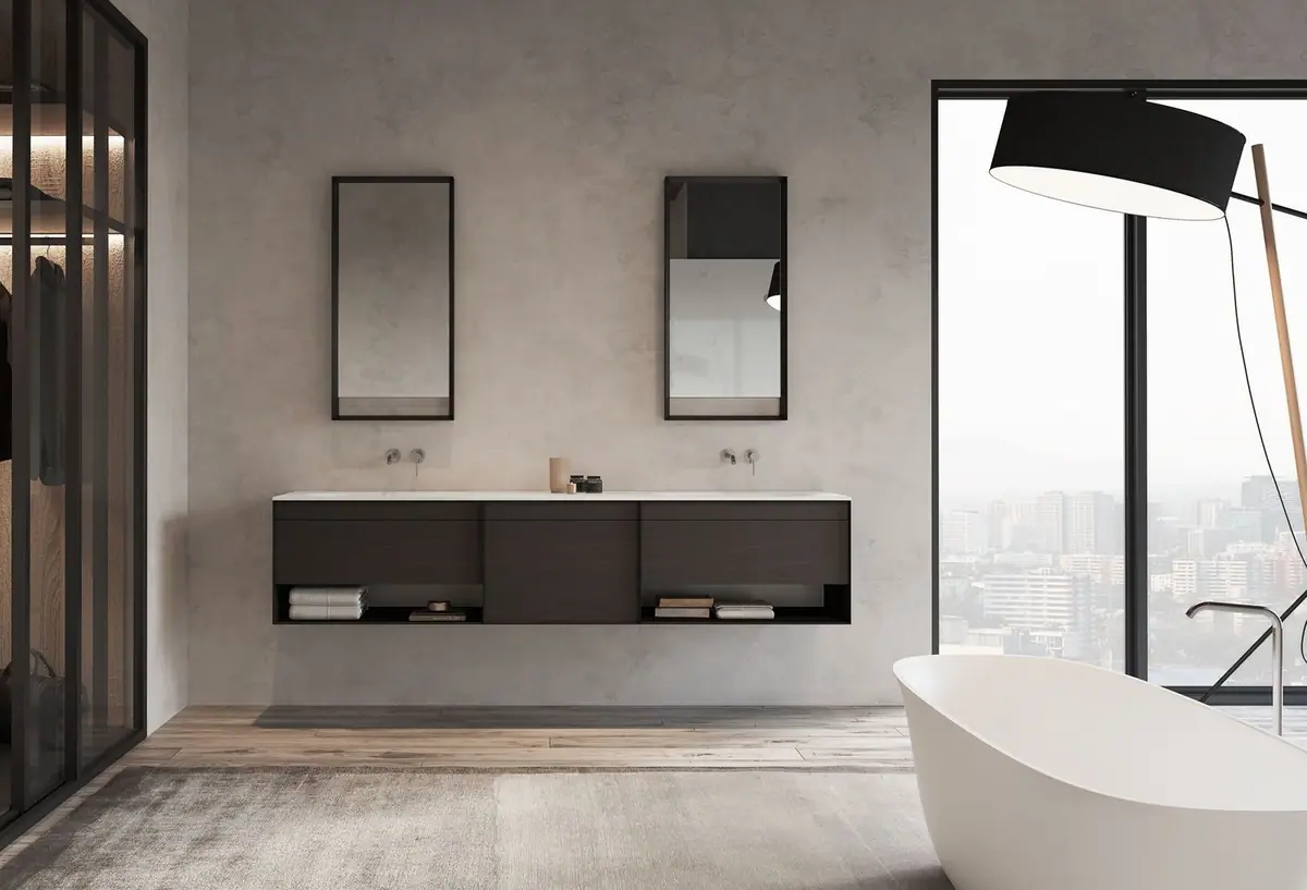 Mueble suspendido oscuro de tres cuerpos con huecos abiertos, dos espejos de marco negro y una bañera exenta junto a un ventanal.