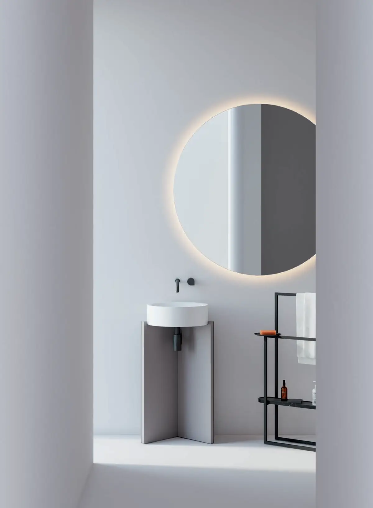 Lavabo de pie gris con lavabo circular blanco, espejo redondo retroiluminado y toallero autoportante negro.