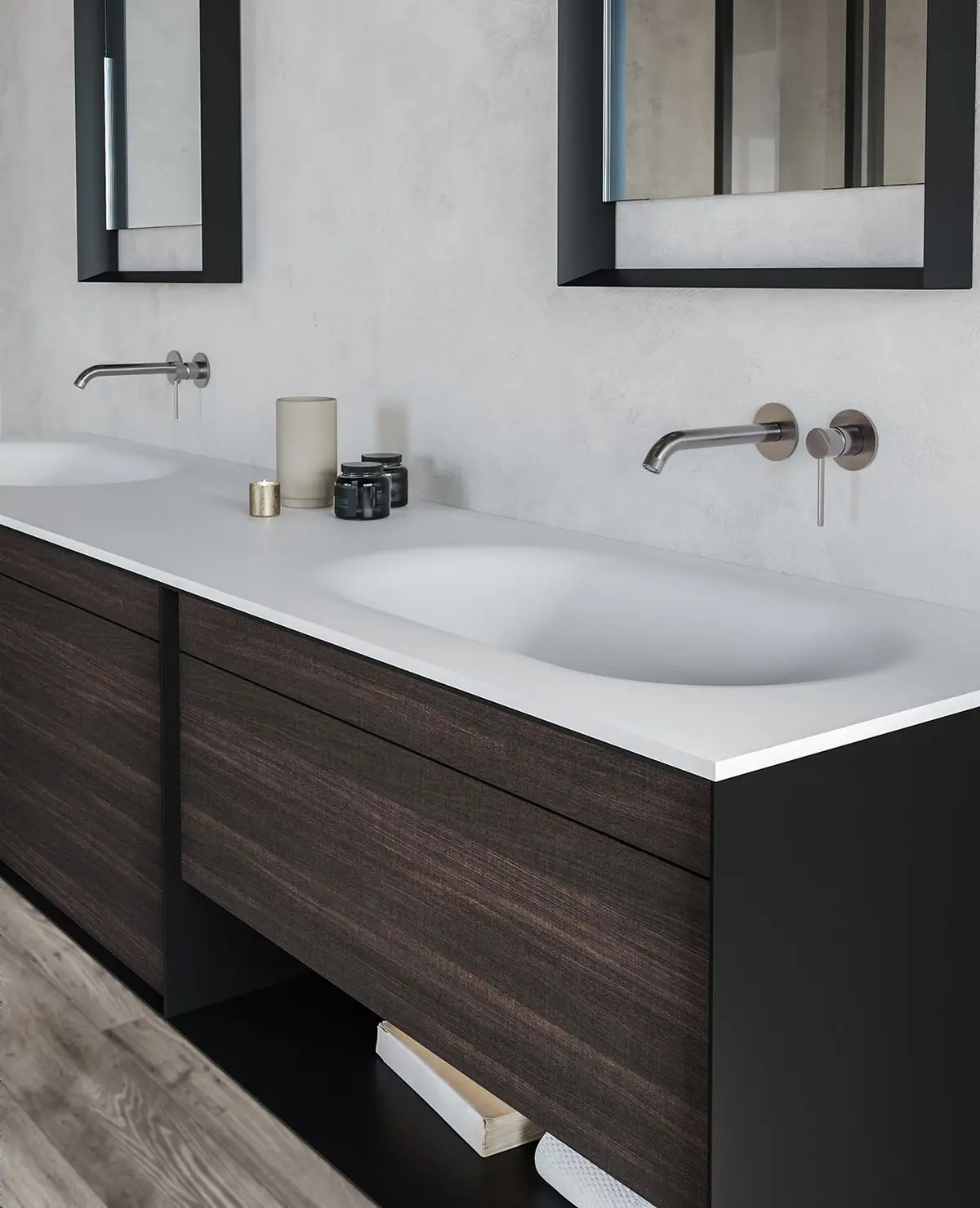 Mueble suspendido con frentes de madera oscura, encimera blanca con dos lavabos integrados y espejos de marco negro.