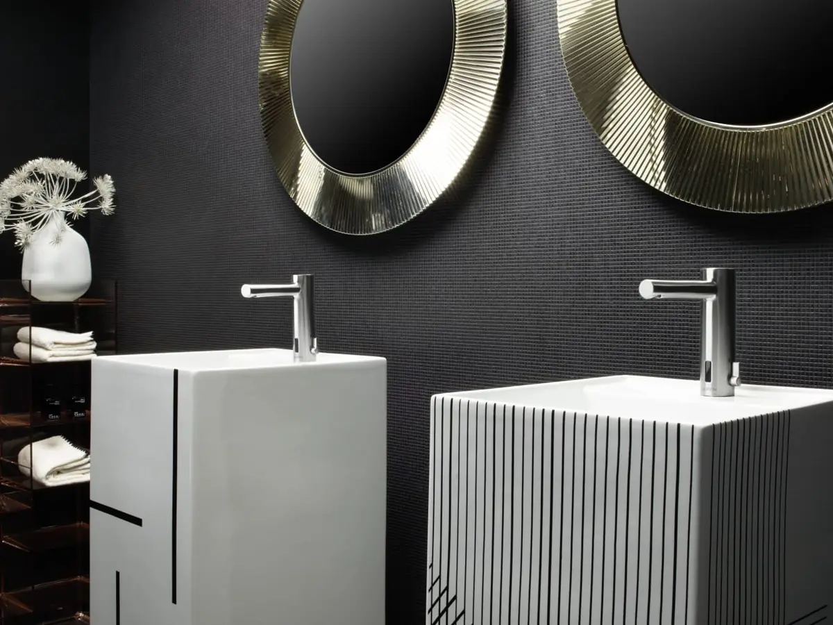 Dos lavabos de pie blancos con decoraciones de líneas negras bajo dos espejos redondos dorados