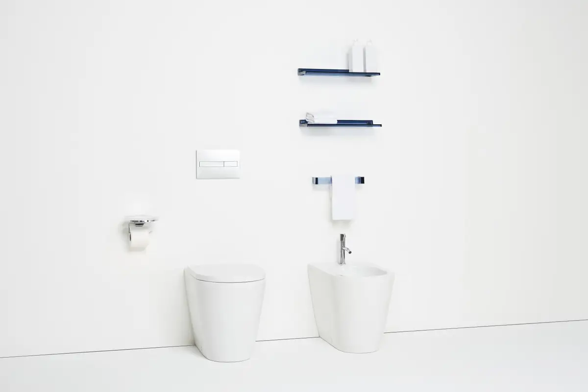 Inodoro y bidé de pie blancos con estantes y toallero transparentes azules en la pared