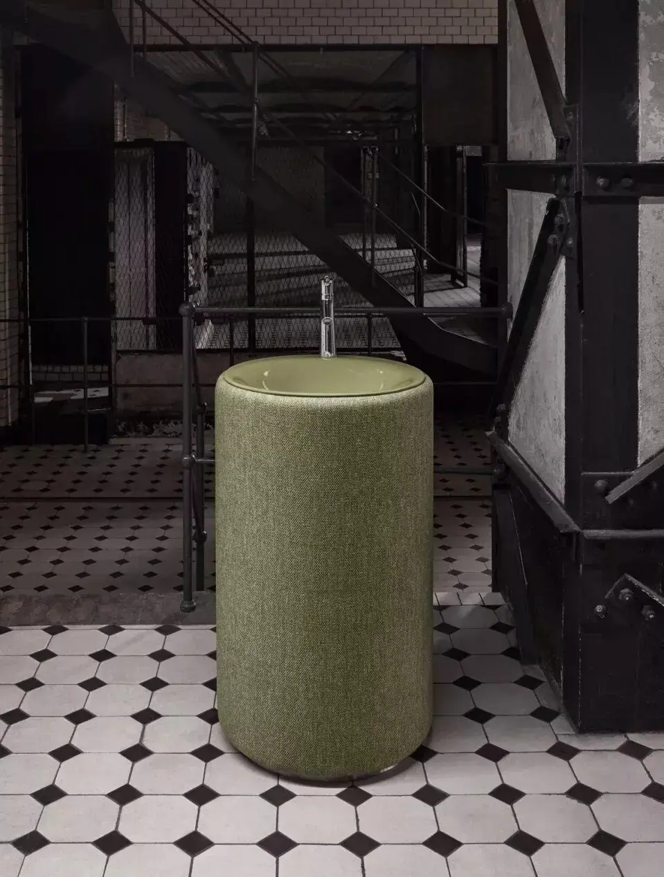 Lavabo de pie cilíndrico tapizado en tejido verde con cubeta esmaltada del mismo tono y grifo cromado, en un interior industrial