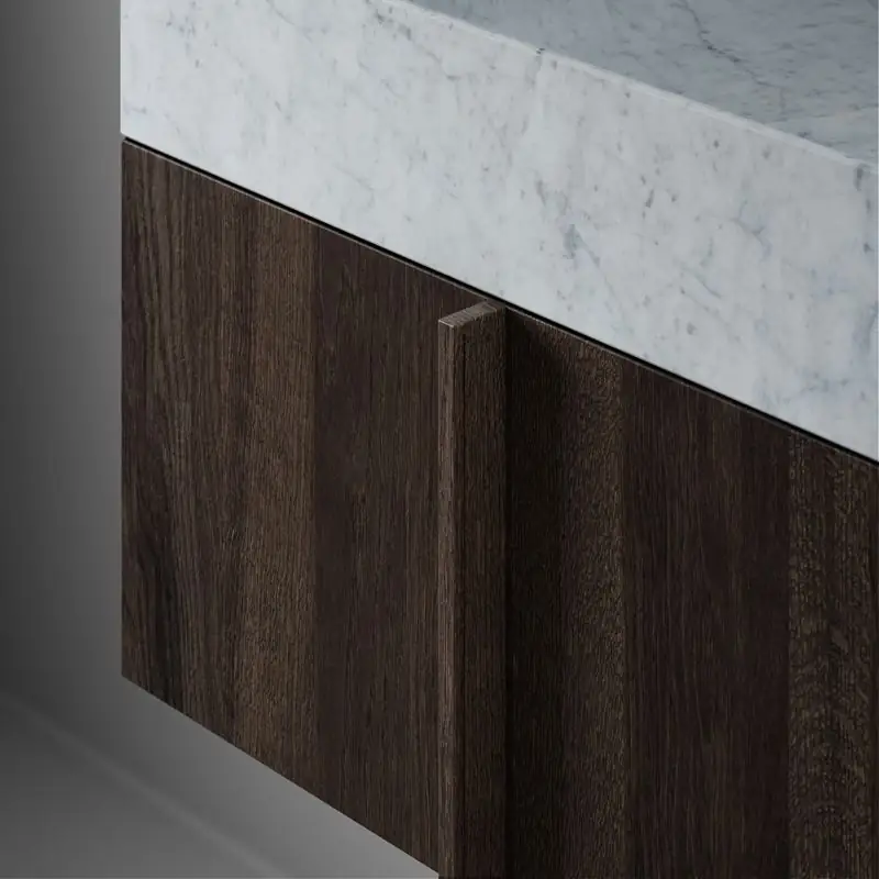 Detalle de un lavabo de mármol blanco veteado sobre un módulo de roble oscuro con tirador vertical de la misma madera.