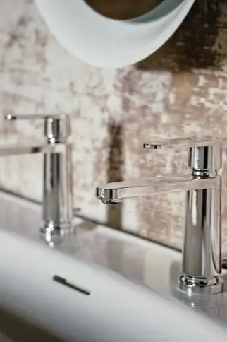 Detalle de dos grifos monomando cromados de cuerpo cónico junto a un lavabo blanco