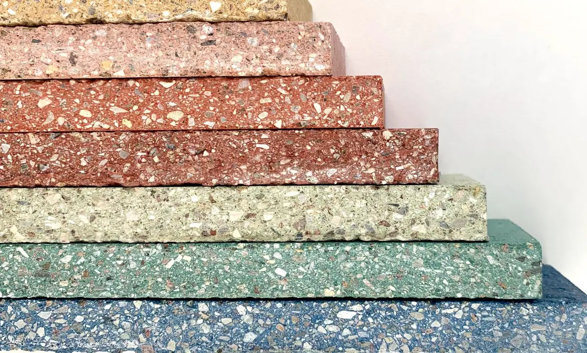 Piezas de piedra compactada de distintos colores apiladas, con el árido visible en el canto