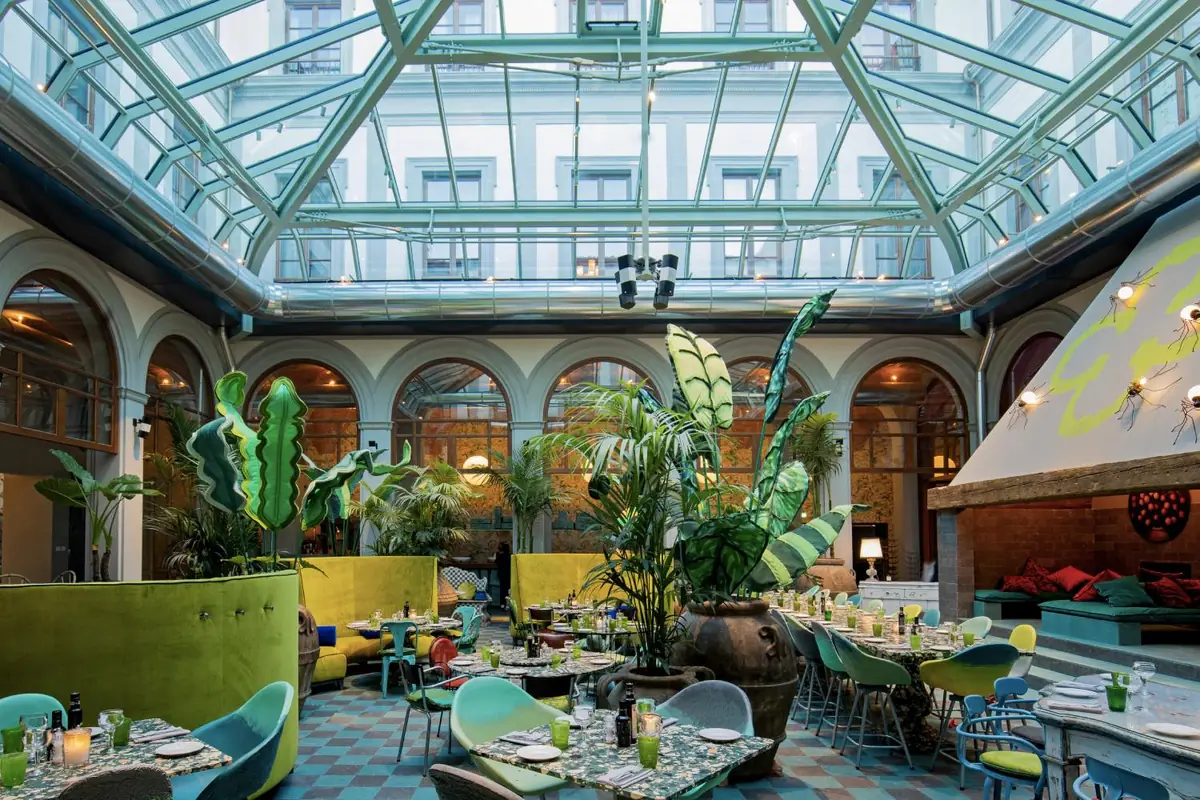 Patio cubierto de un hotel con restaurante y suelo ajedrezado de piedra compactada en tonos verdes y azules