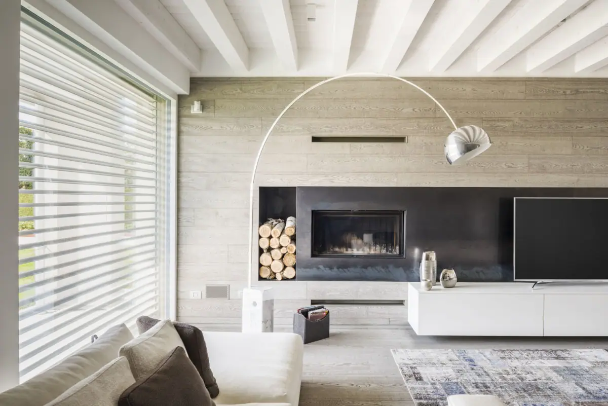 Sala de estar con una pared revestida de tablas de roble claro, chimenea empotrada en un frente negro y suelo de madera