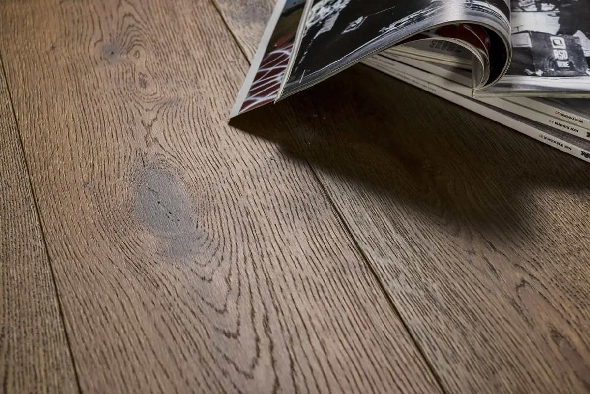 Tablas anchas de roble cepillado de tono pardo grisáceo con unas revistas apoyadas en el suelo