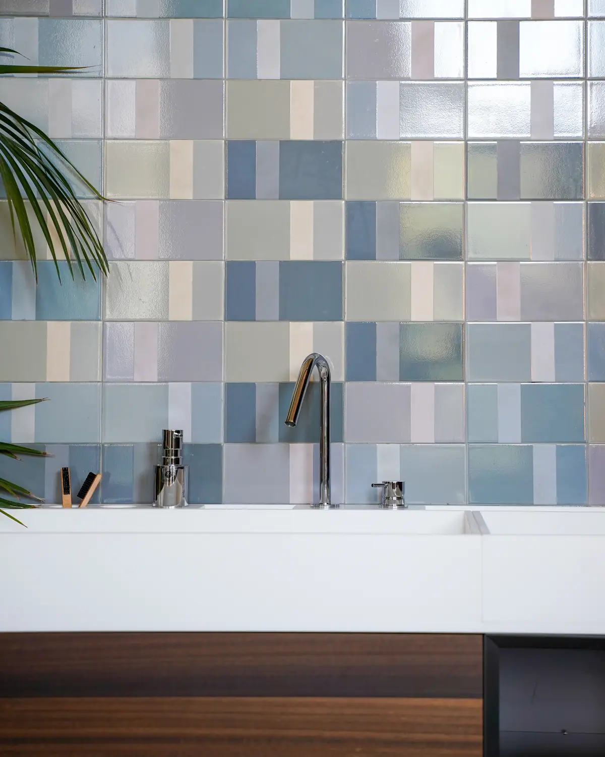 Lavabo blanco con caño alto cromado y mando independiente, frente a una pared de azulejos en tonos azules y grises.