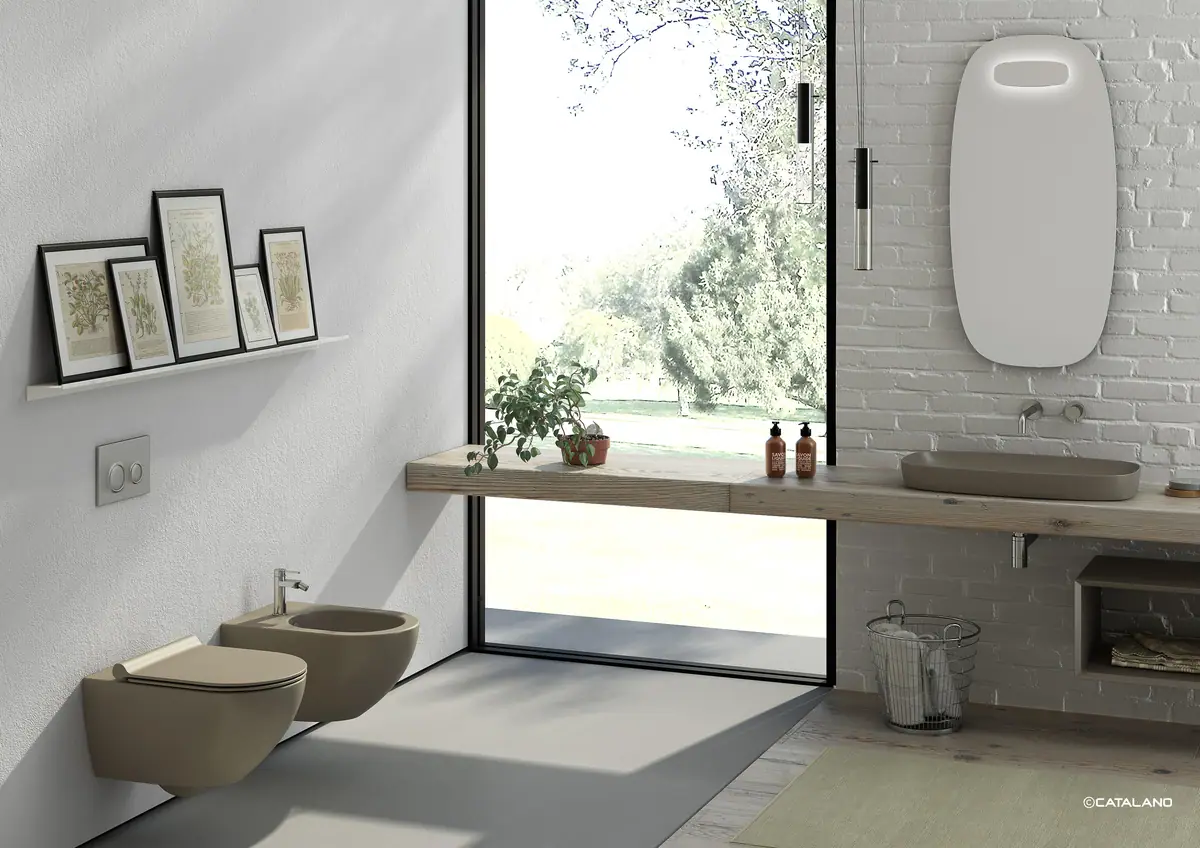 Baño con un lavabo marrón satinado sobre una encimera de madera junto a una ventana y un inodoro y un bidé suspendidos del mismo color