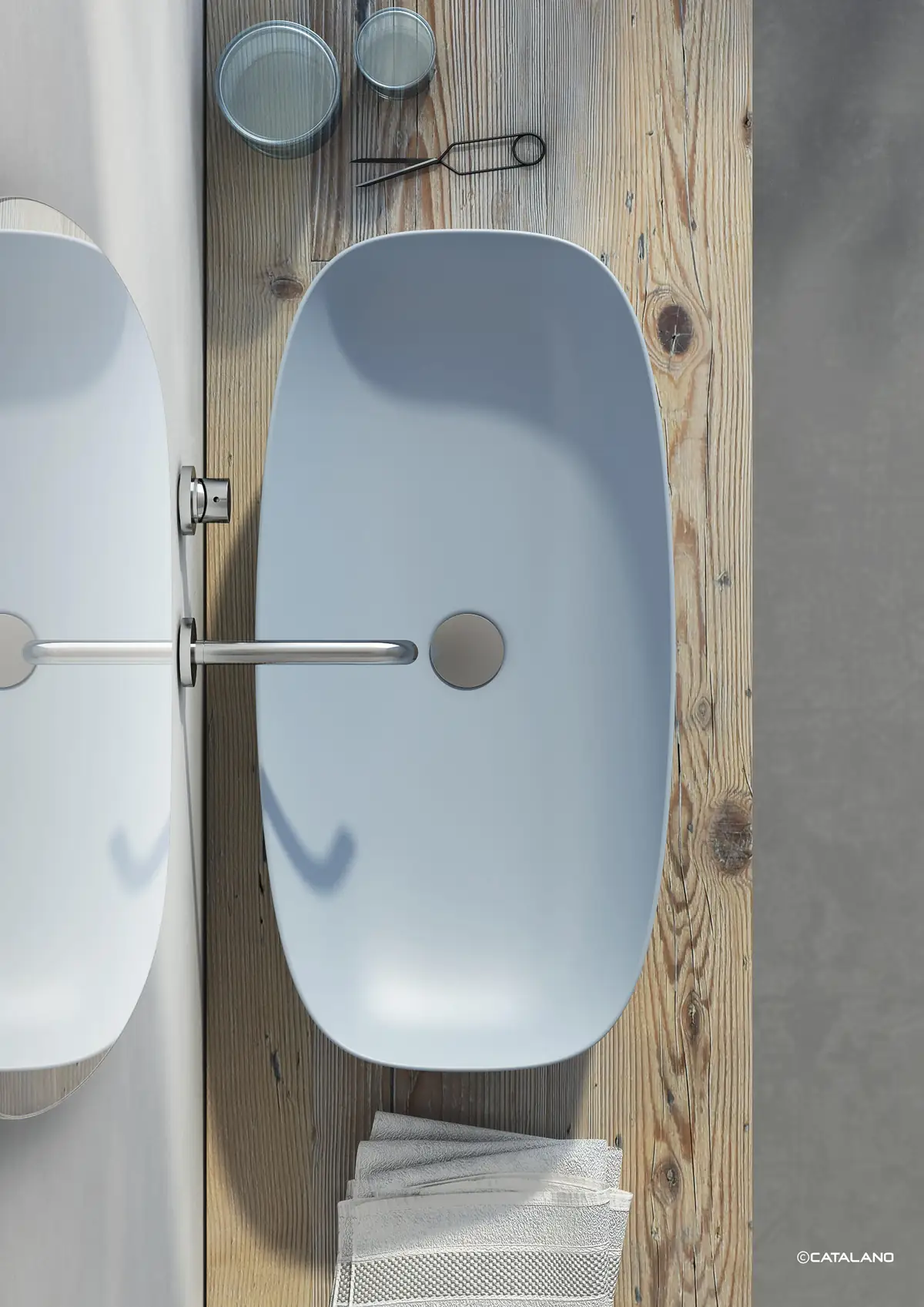 Vista cenital de un lavabo azul de cubeta amplia sobre una encimera de madera, con grifería mural de acero