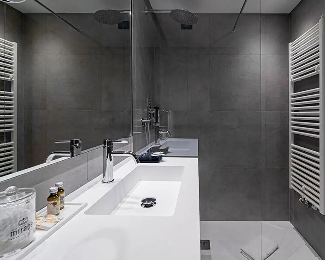 Baño con encimera blanca de lavabo integrado, grifería cromada, espejo y paredes de porcelánico gris oscuro