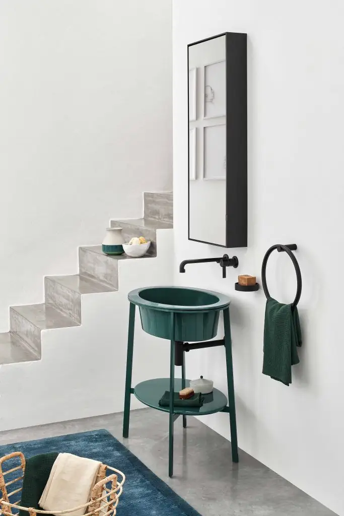 Lavabo redondo verde sobre estructura metálica verde con estante del mismo color, junto a una escalera