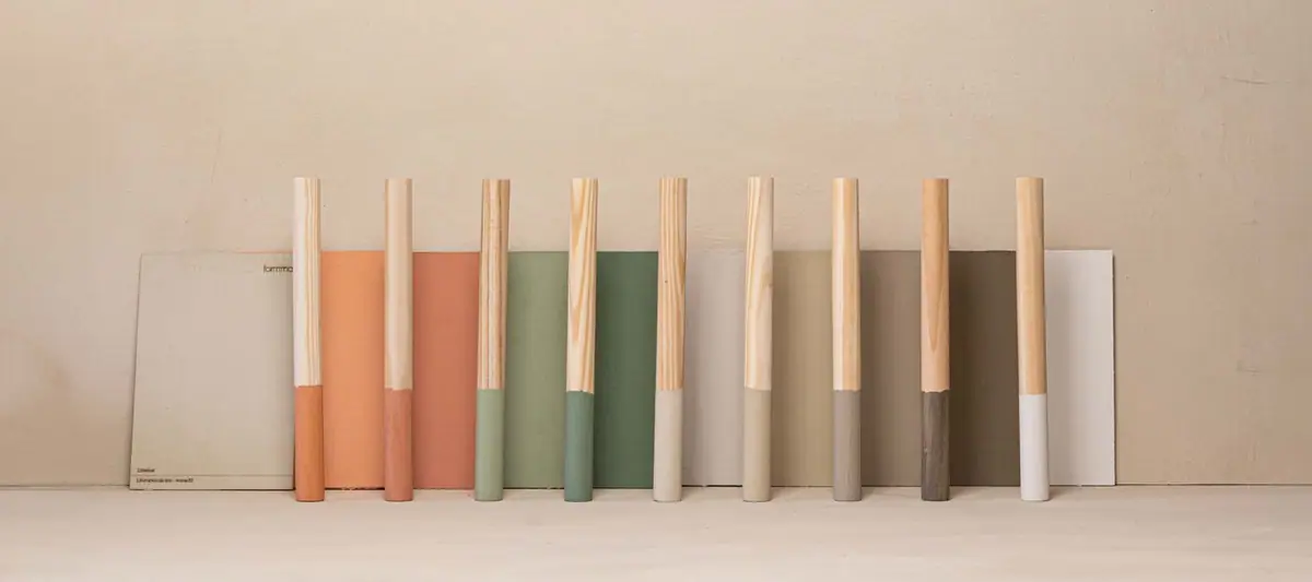Varillas de madera con el extremo pintado en terracota, verde, arena, gris y blanco apoyadas en muestras de pintura del mismo color