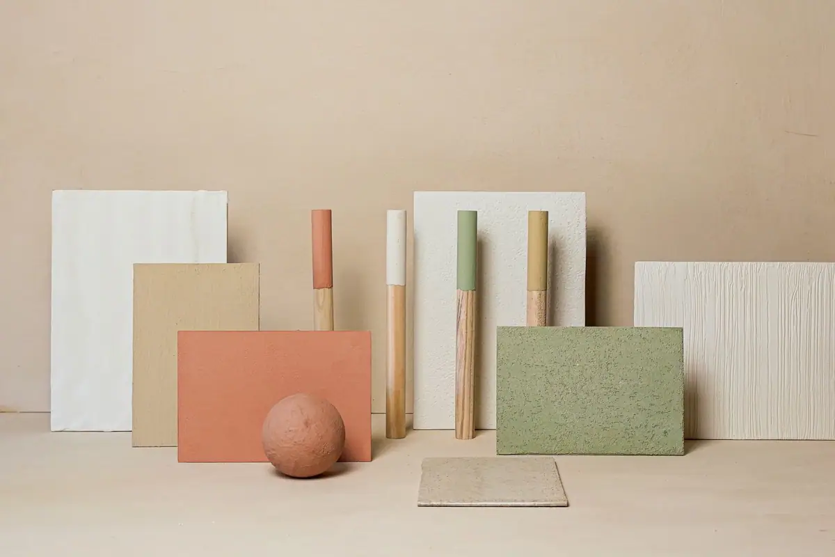 Muestras de revestimientos de cal en blanco, arena, terracota y verde junto a varillas de madera pintadas y una esfera texturada