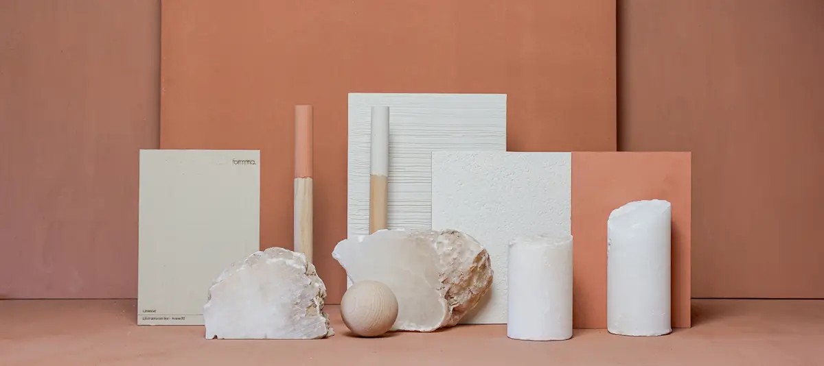 Composición de muestras de estuco de cal en blanco y terracota con piedras, cilindros y una esfera de madera sobre fondo terracota