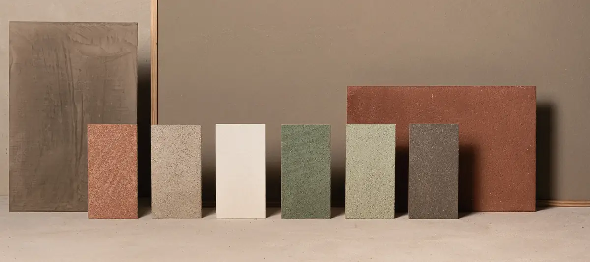 Muestras rectangulares de revestimiento de cal en terracota, arena, blanco, verdes y gris oscuro ante un fondo pintado