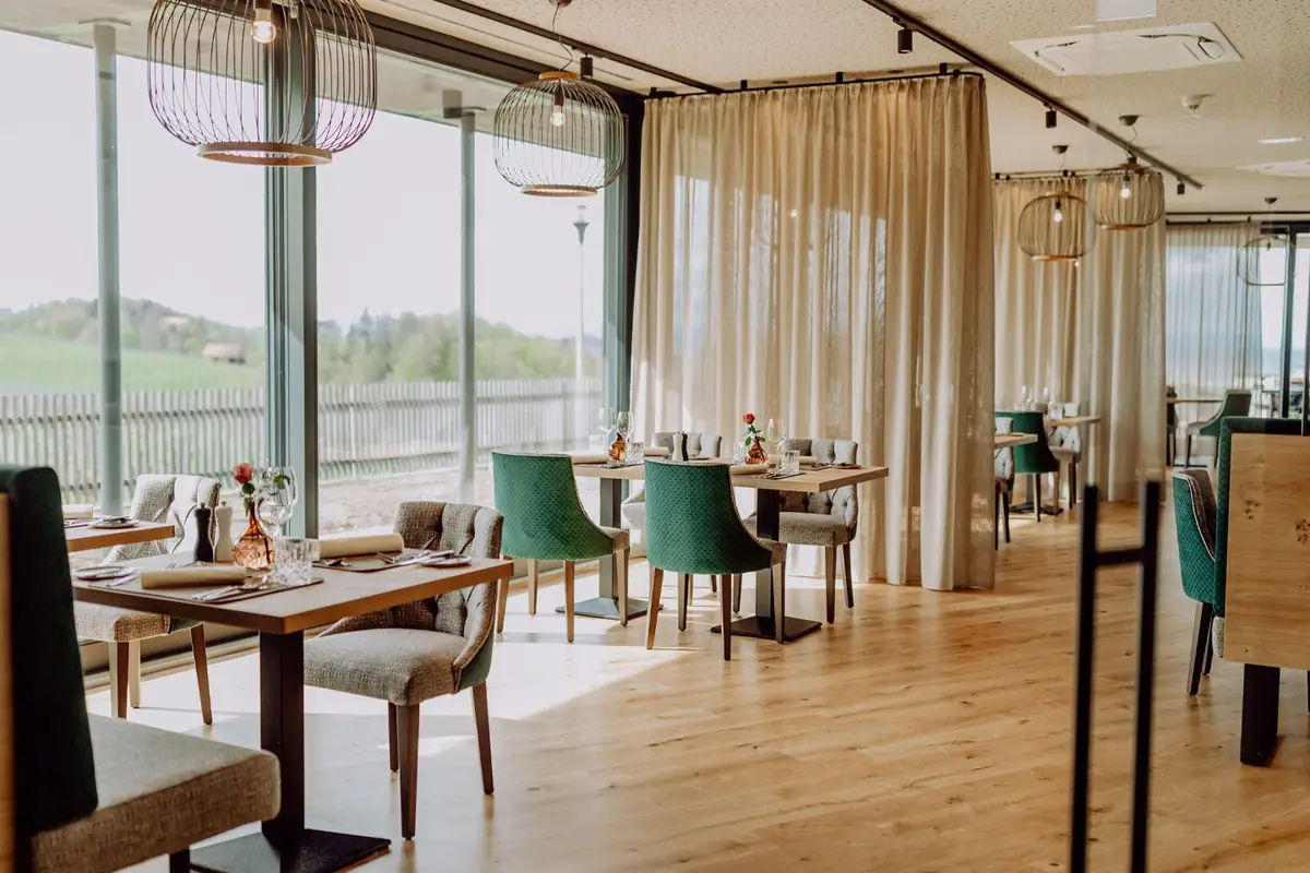 Comedor de restaurante con suelo de tablas de roble claro, mesas de madera y grandes ventanales abiertos al paisaje