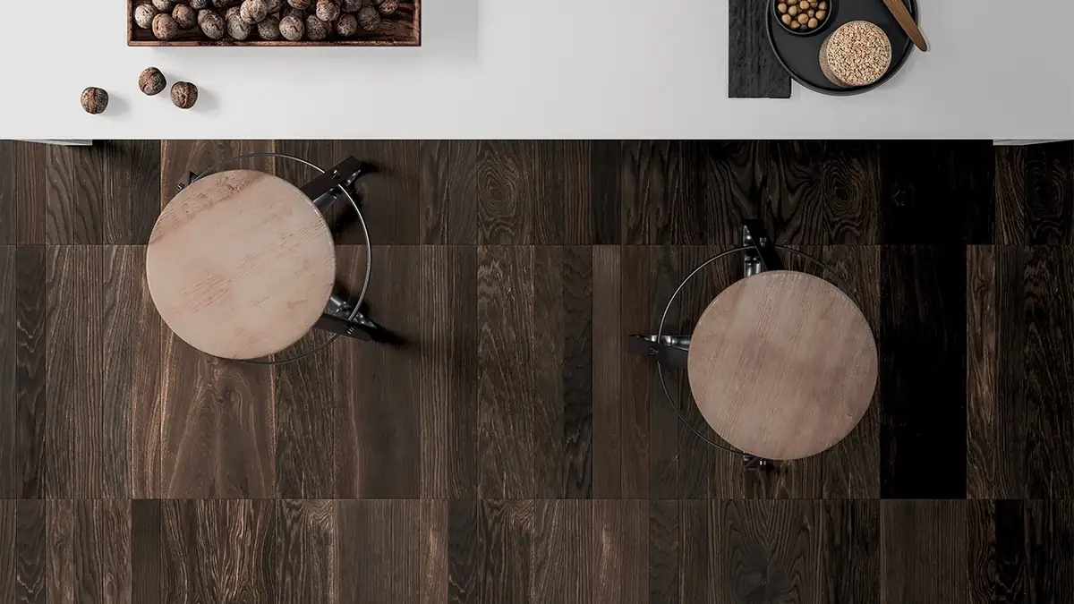 Vista cenital de un suelo de tablas de madera oscura con dos taburetes de asiento de madera junto a una encimera blanca