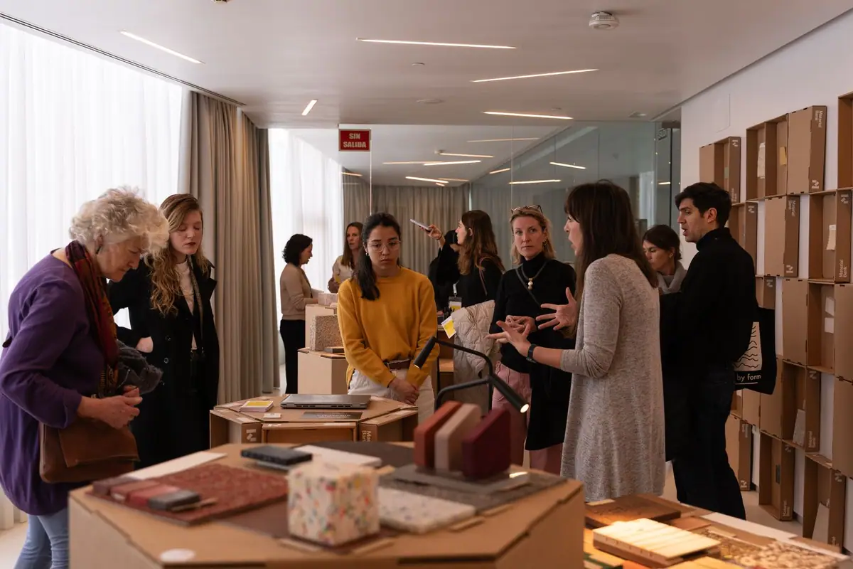 Visitantes conversan alrededor de una peana con muestras de materiales en la sala de la exposición