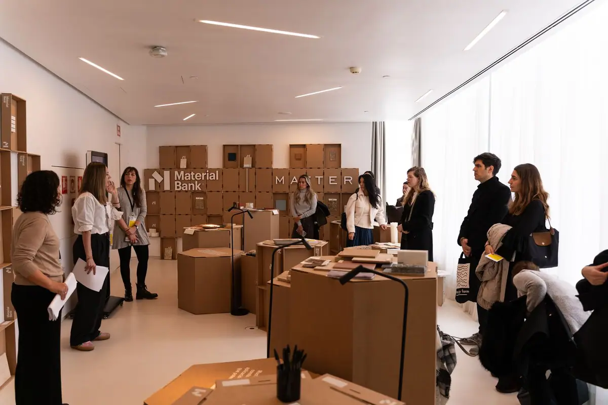 Una consultora explica la exposición a un grupo de visitantes ante un muro de módulos de cartón con los logotipos de Material Bank y Matter