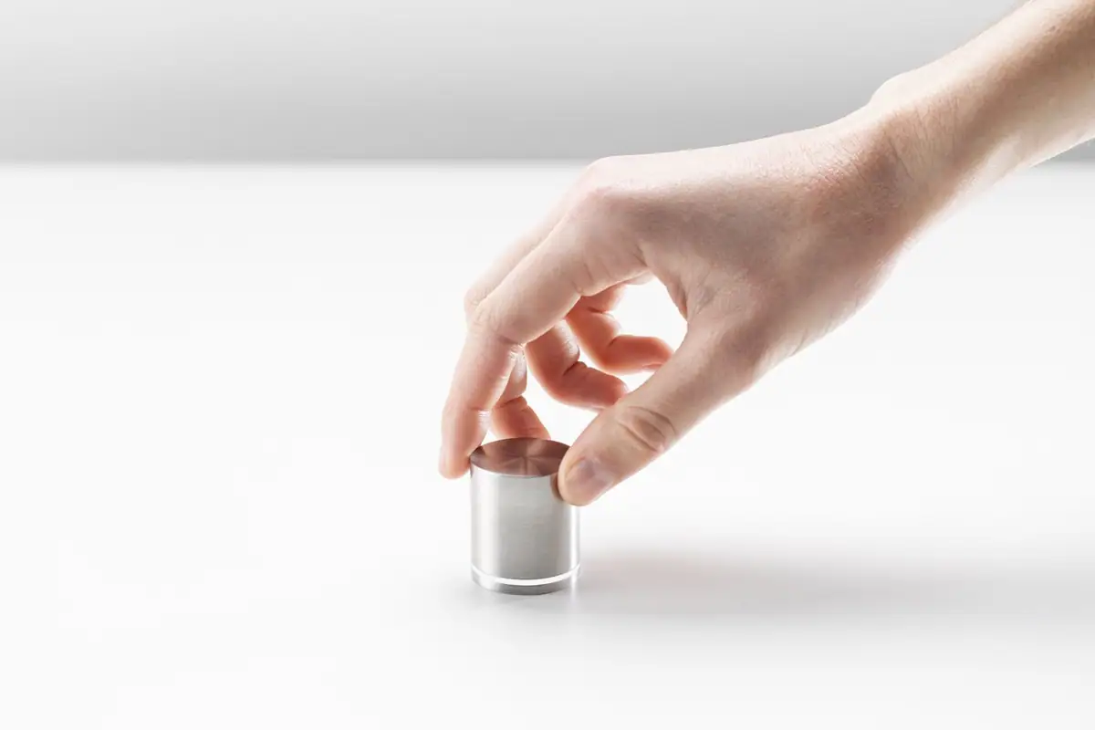 Mano girando un mando cilíndrico de acero inoxidable sobre una superficie blanca